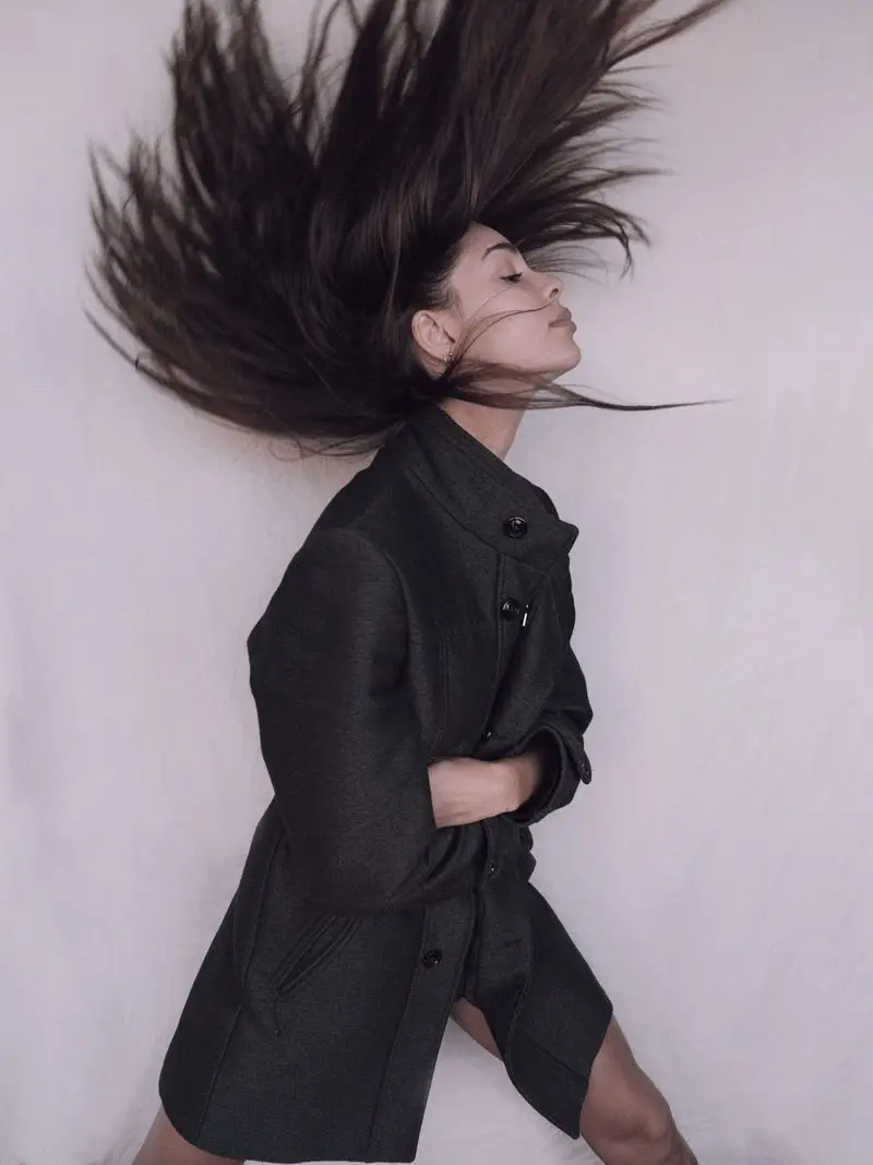 Dark hair thrown up mid-movement against a pale wall